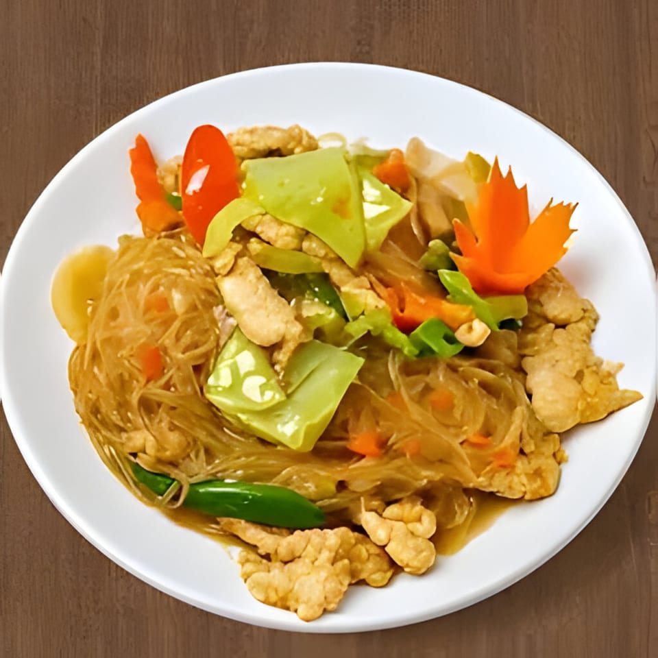 Thai glass noodles with chicken, green peppers, carrots, and a carved carrot garnish on a white plate.