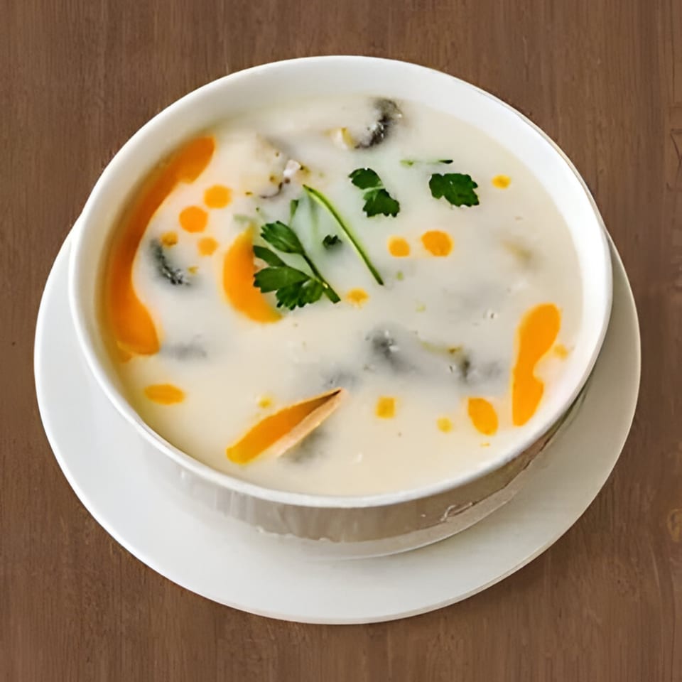 Creamy Thai soup with mushrooms, orange oil, and fresh parsley in a white bowl.