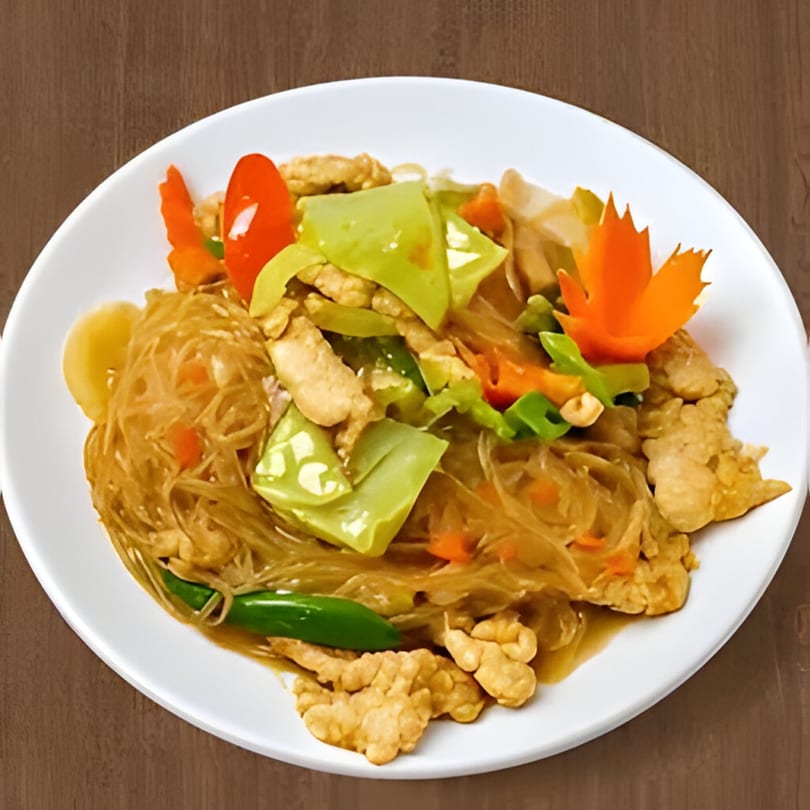 Thai glass noodles with chicken, green peppers, carrots, and a carved carrot garnish on a white plate.